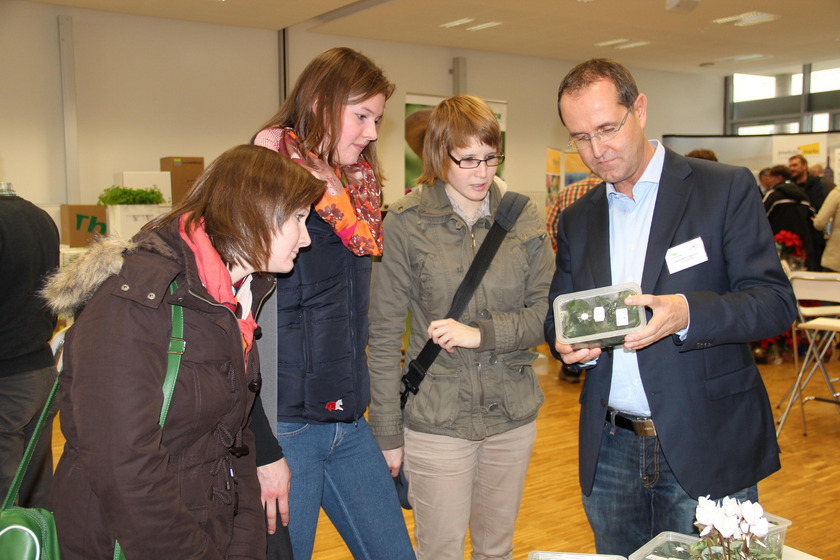 Auf dem Bild sieht man drei junge Frauen und einen Mann. Der Mann hat ein Kästchen mit grünen Plfanzen in der Hand. Alle schauen darauf.