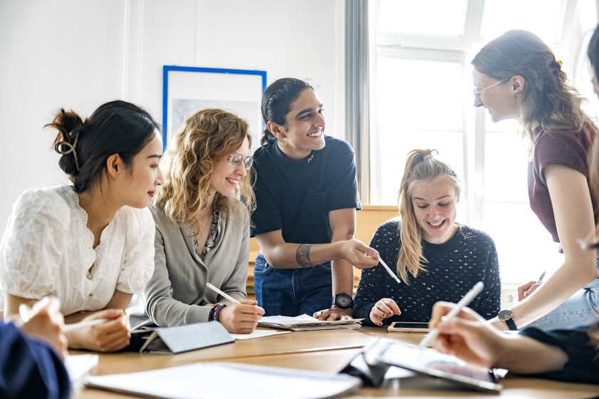 Vier Studentinnen und ein Student sitzen gemeinsam am Tisch und diskutieren