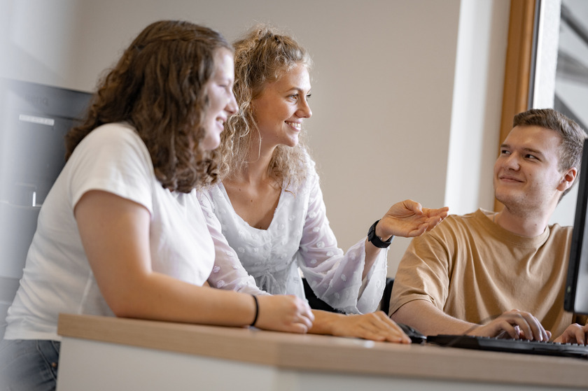 Drei Studierende sitzen gemeinsam an einem Tisch und diskutieren 